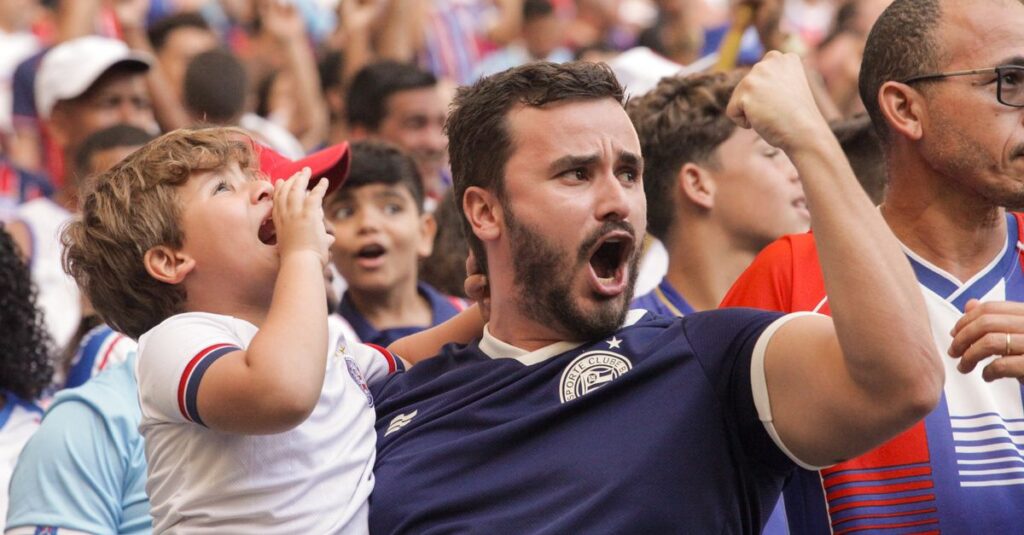 O calendário do futebol brasileiro em 2026 Um pai e seu filho torcendo em um jogo de futebol, expressando alegria e emoção.